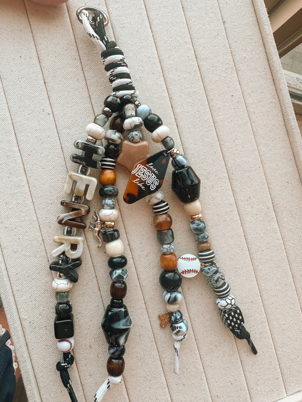 A black, white and wood-bead Lucky Loop charm spelling Henry with a baseball charm