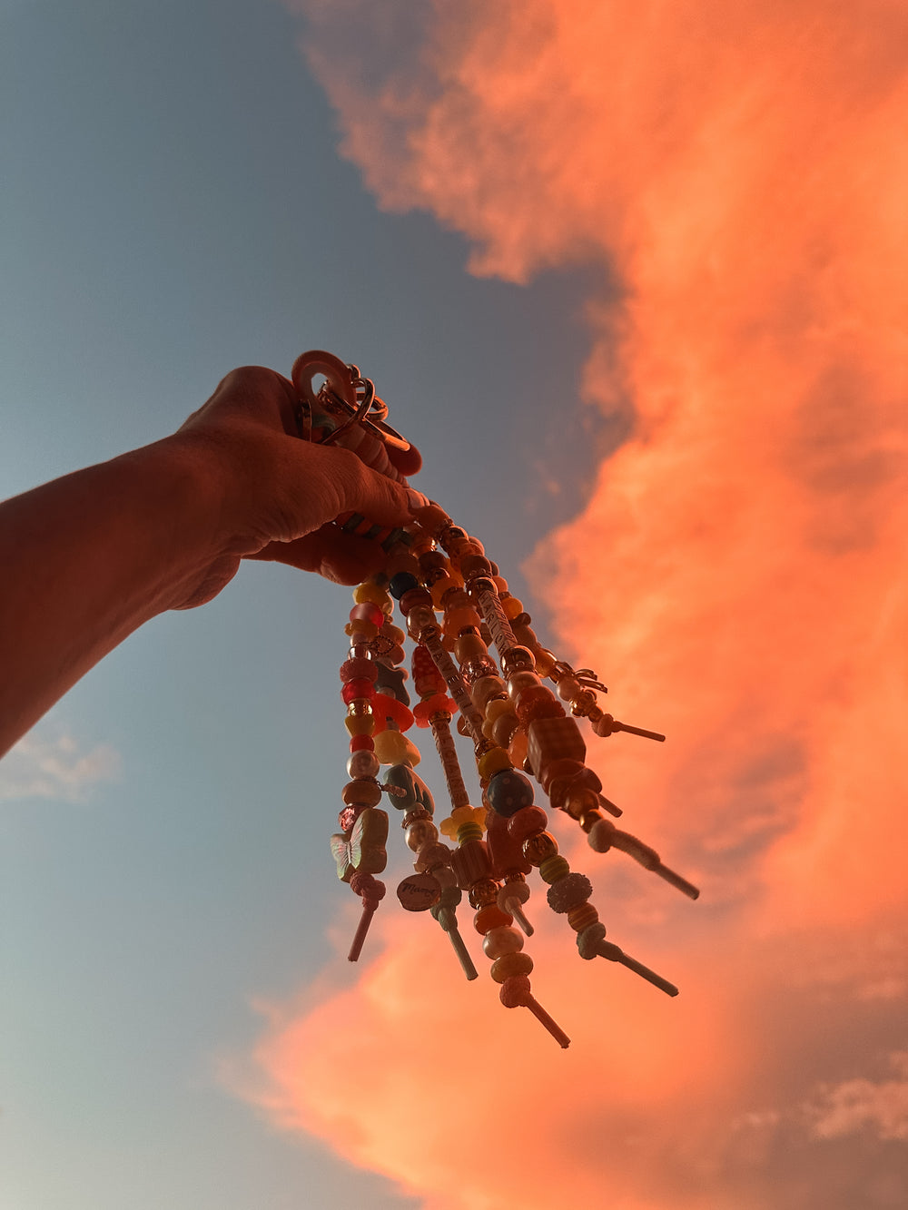 A handful of Lucky Loop bag charms held up against an orange sunset sky