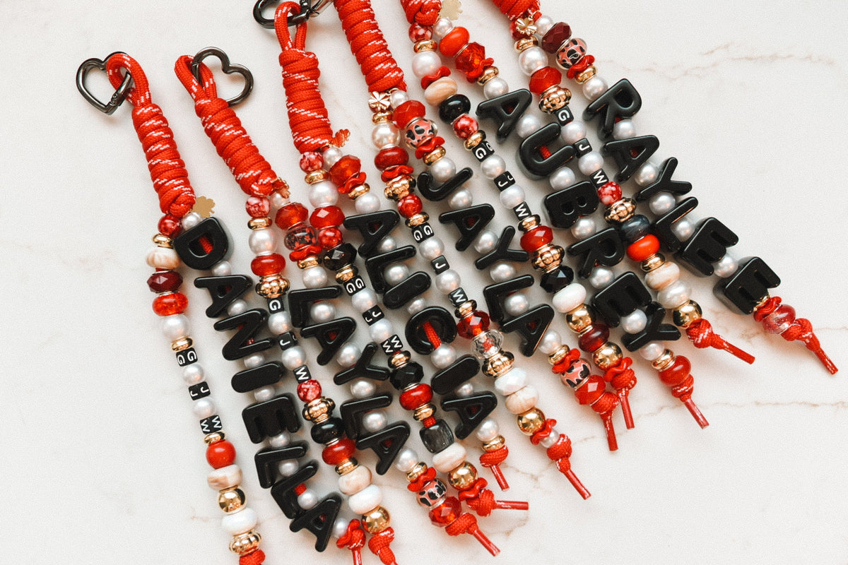 Six matching Lucky Loop bag charms in red and black team colors, each beaded with a different name