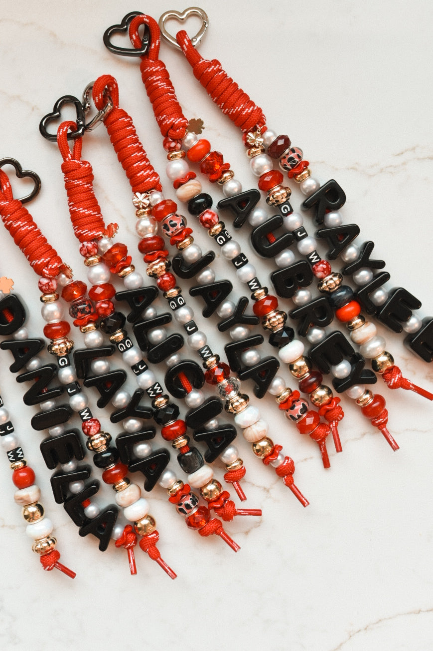 Red and black personalized bag charms clipped together, names spelled in black letter beads