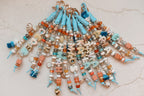 A group of coastal blue Lucky Loop bag charms fanned out from their heart clasps, each spelling a different name