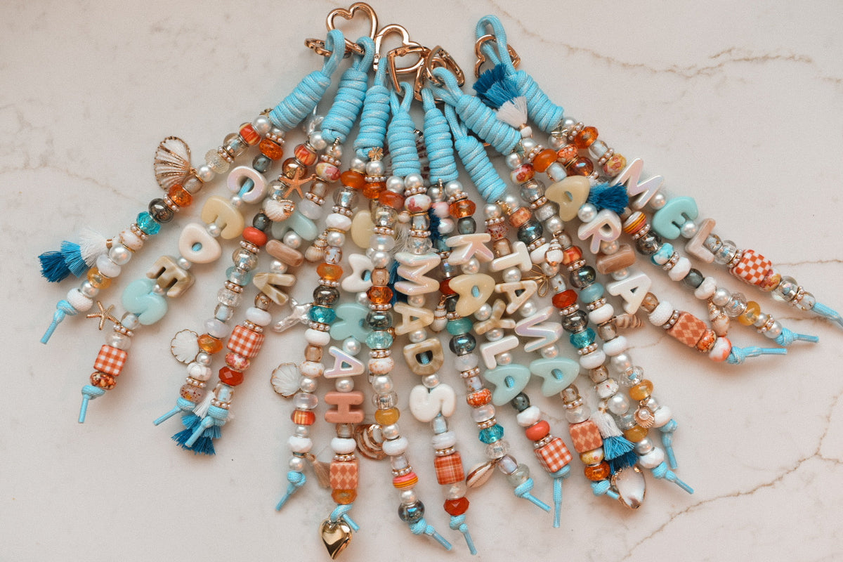 A group of coastal blue Lucky Loop bag charms fanned out from their heart clasps, each spelling a different name