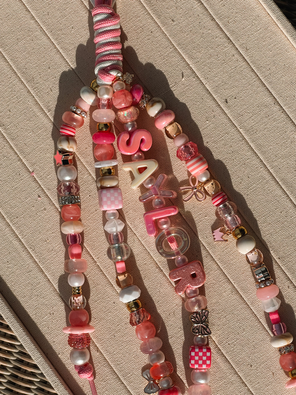 A pink Lucky Loop charm spelling Sailor in bright sunlight