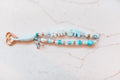 Amen 2-strand loop in sky blue and aqua with AMEN letter beads, a blue floral bow charm, a gold cross and a rose gold heart clasp