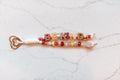 Be Kind 2-strand loop in cherry red, honey and cream with BE KIND letter beads, a gingham cube, a golden bee charm and a rose gold heart clasp