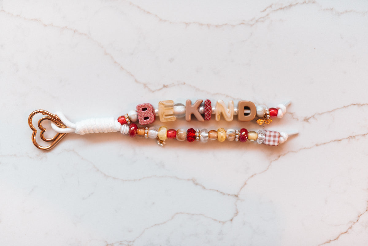 Be Kind 2-strand loop in cherry red, honey and cream with BE KIND letter beads, a gingham cube, a golden bee charm and a rose gold heart clasp