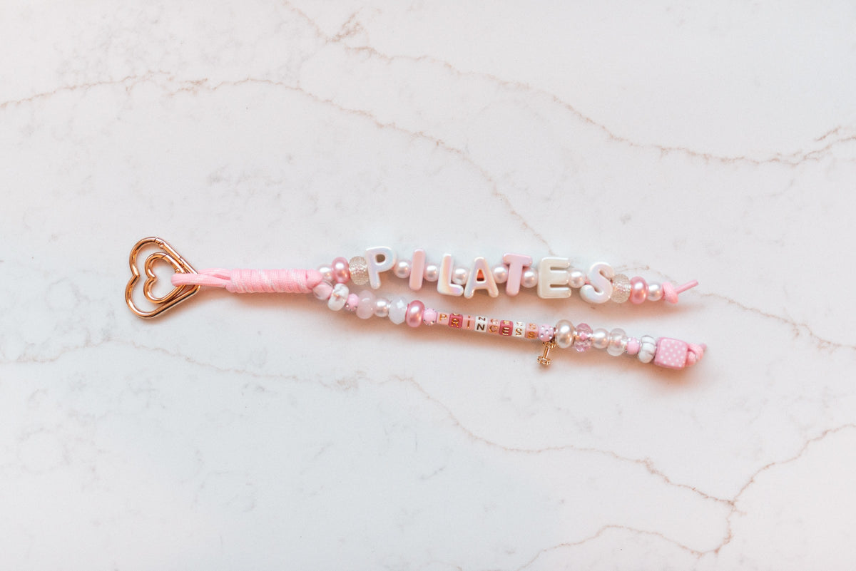 Pilates Princess loop — pink and pearl 2-strand bag charm spelling PILATES and PRINCESS on a rose gold heart clasp