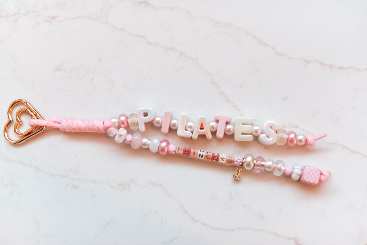 Pilates Princess loop close-up showing iridescent PILATES letters and a gold dumbbell charm